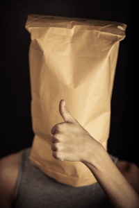 Preteen boy covering his face with a paper bag and showing thumbs up